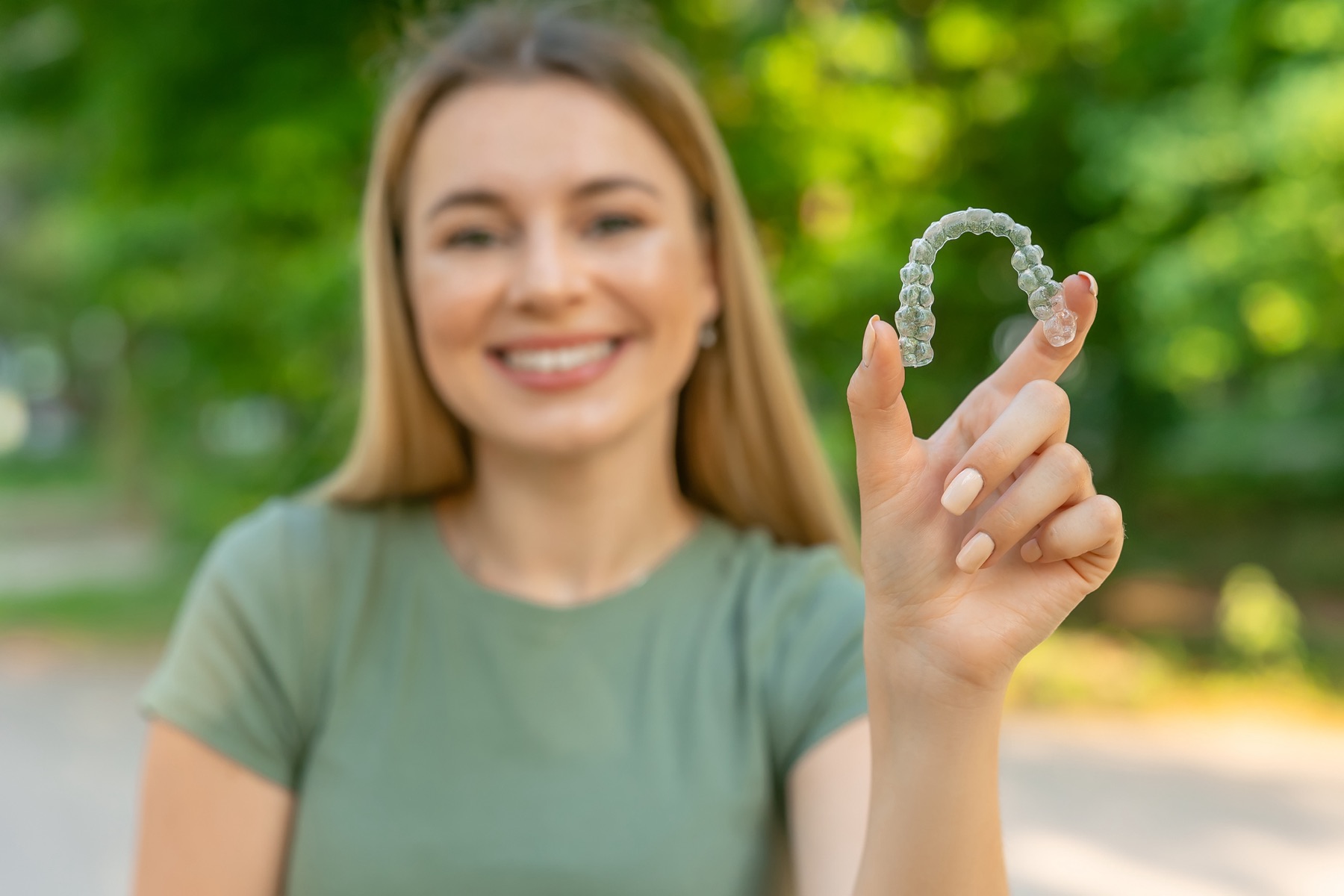 A woman in a park holds up her clear Invisalign® tray